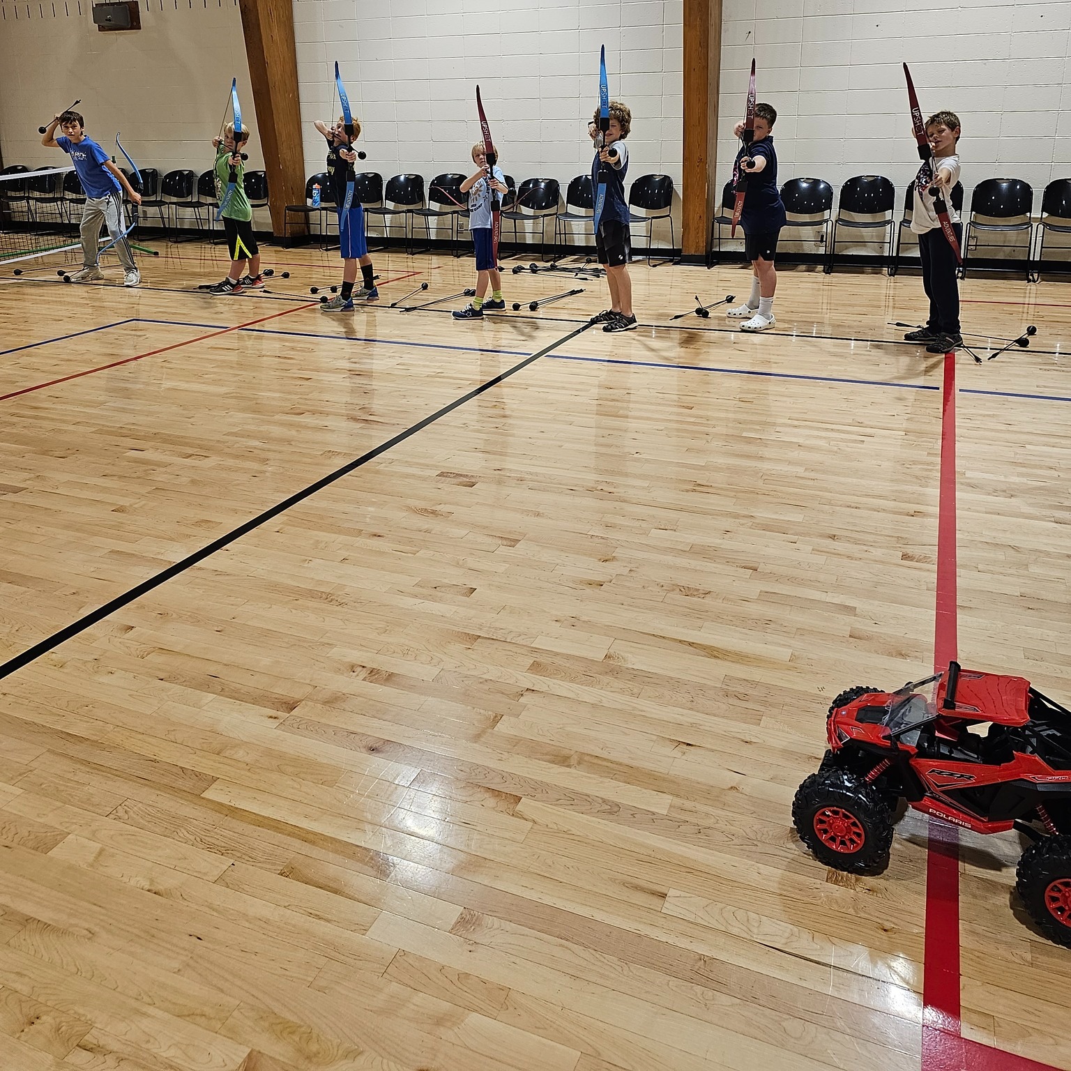 Kids at foam-tipped archery station with an RC car nearby