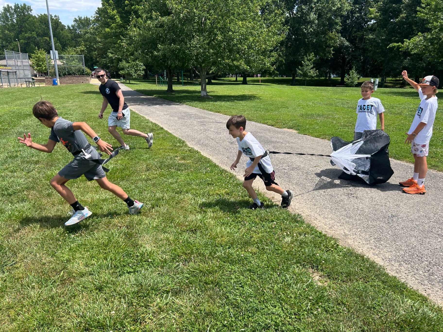 Kids sprinting with resistance parachutes during a Recreation Academy flag football camp